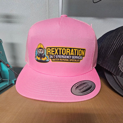 A bright pink snapback trucker hat with a yellow and black 'REXTORATION' logo on the front, displayed on a wooden table.